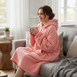Coral pink oversized hooded blanket with a large kangaroo front pocket worn seated on a sofa