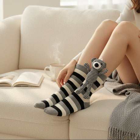 Person wearing striped socks with a small plush teddy, sitting on a couch with a book and cup