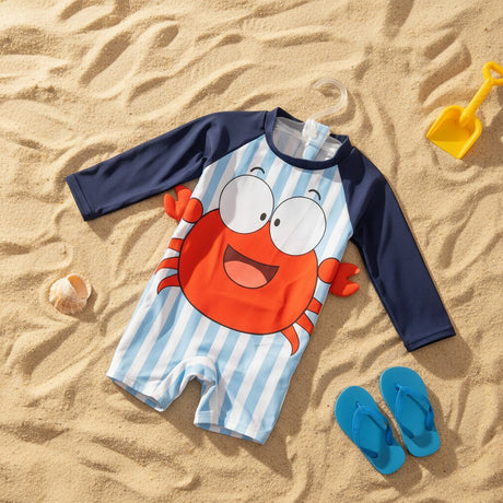 A children's long-sleeve one-piece swimsuit laid flat on sandy ground with beach props