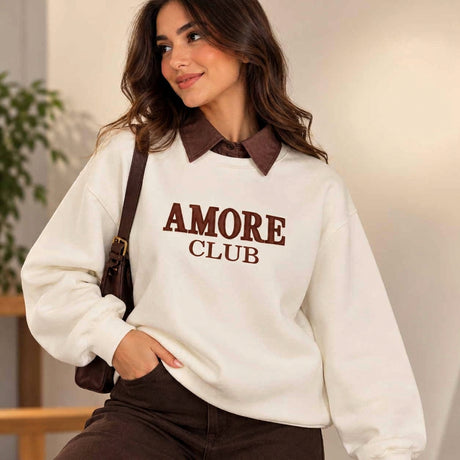 Woman in a cream Amore Club sweatshirt with brown embroidery over a brown collared shirt