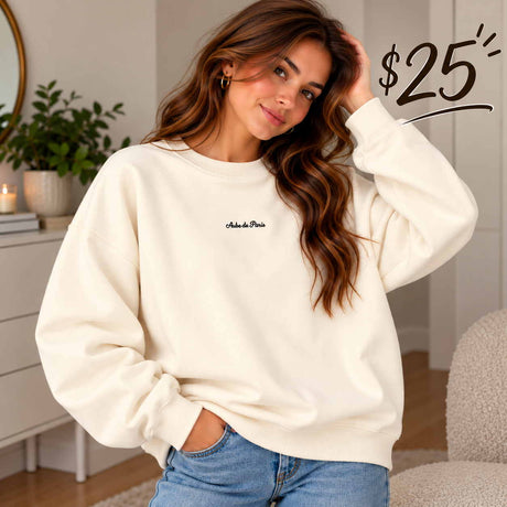 Close crop of a cream Aube de Paris sweatshirt with dropped shoulders, worn with relaxed jeans