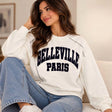 Woman in a cream Belleville Paris sweatshirt with navy lettering and contrast stitched seams