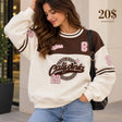 Woman in a cream and brown varsity sweatshirt with a chenille California patch and pink 23 numbers