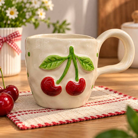 Glossy red cherries on a green stem sculpted onto a cream mug, fresh cherries beside it