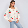 Woman in a cream knit cardigan with red cherries and three bow ties over a white top and light blue jeans