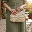 Cream and tan crochet clutch bag held in green dress outdoors, Jack Gifts Online Lebanon