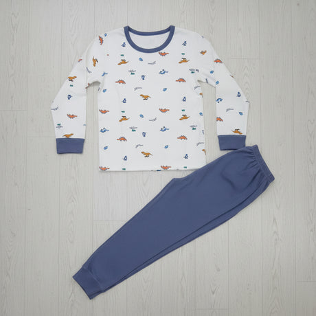 Cream dinosaur print pyjama top with slate blue joggers laid flat on a wood floor