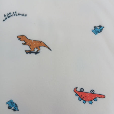 Close up of skateboarding dinosaur print in orange, red and blue on cream pyjama fabric