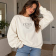 Woman in a cream crew neck sweatshirt with minimalist Fiore lettering, worn with light jeans