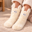 Shaggy cream fluffy socks with upright bunny ears and big round eyes worn on a beige rug