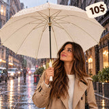 Woman in a beige trench coat holding a cream umbrella with gold tips and a white handle in the rain