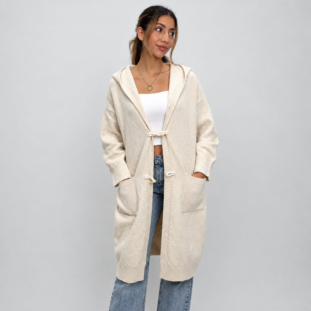 Cream knit toggle cardigan worn open, hands by the pockets