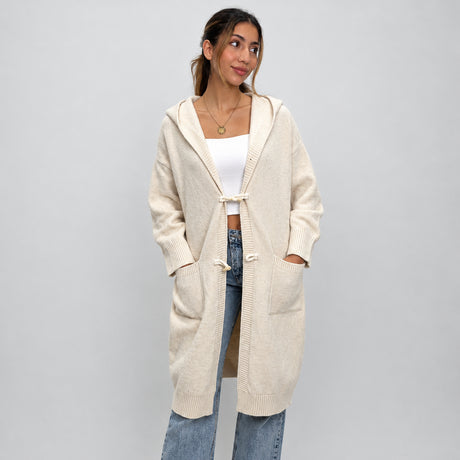 Cream knit toggle cardigan worn open, hands by the pockets