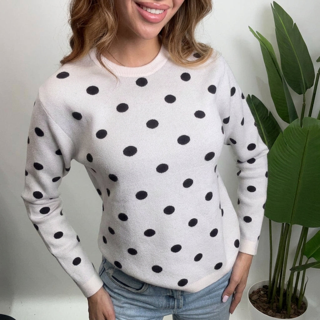 Close up of a cream crew neck sweater with black polka dots and ribbed hem