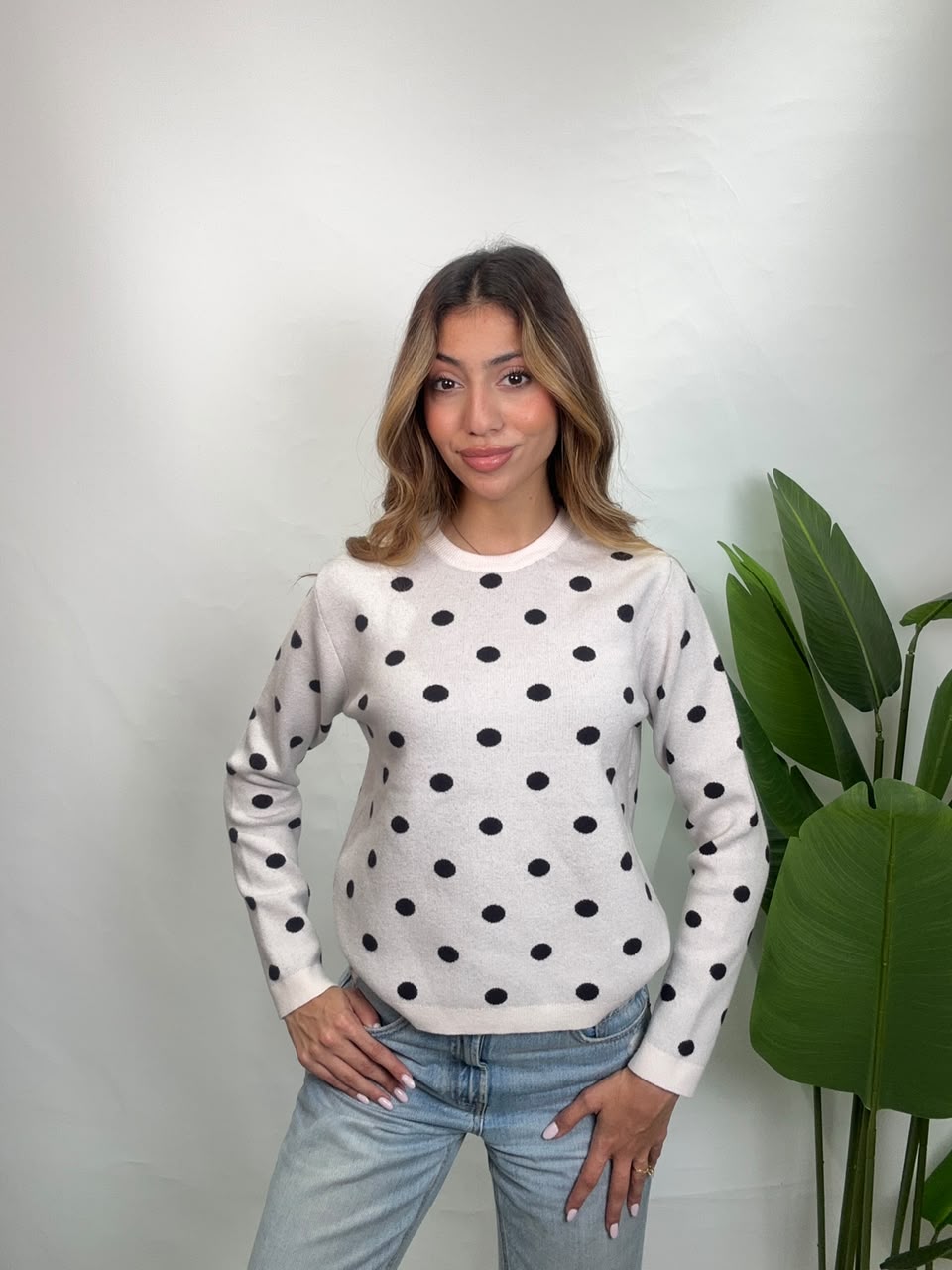 Woman in a cream black polka dot sweater with light blue jeans, both hands on her hips