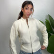 Cream ribbed knit zip up cardigan zipped to the funnel neck, worn with light jeans by a plant