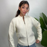 Cream ribbed knit zip up cardigan zipped to the funnel neck, worn with light jeans by a plant
