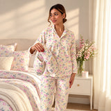 Woman in a cream button up pyjama set with pink roses and yellow blossoms in a sunny bedroom