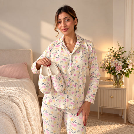 Woman in a cream rose print button up pyjama set holding the matching slippers