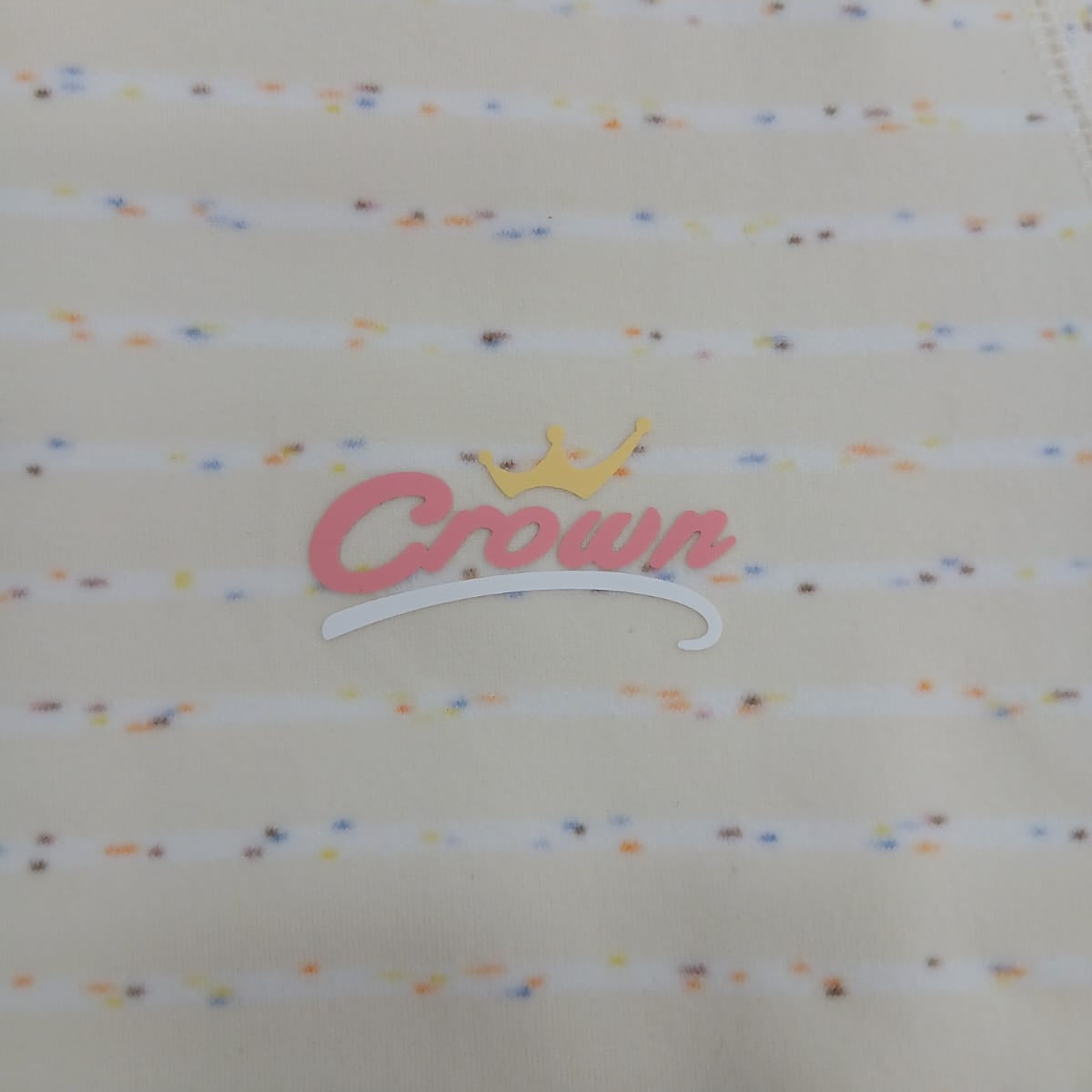 Close up of the pink script chest logo with a gold crown on cream confetti stripe pyjama fabric