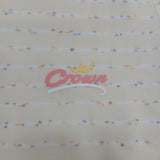 Close up of the pink script chest logo with a gold crown on cream confetti stripe pyjama fabric