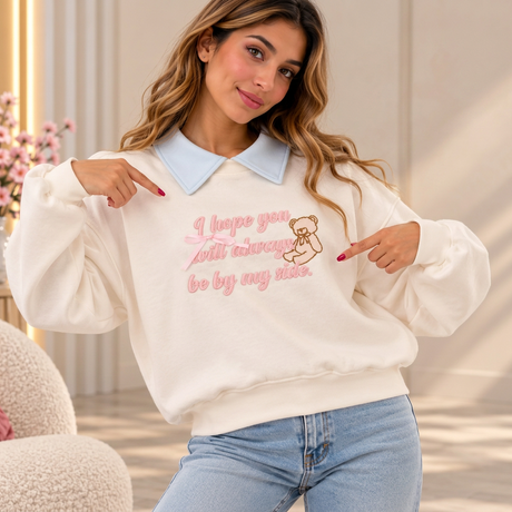 Cream sweatshirt with a baby blue collar, pink script slogan, teddy bear outline and pink satin bow
