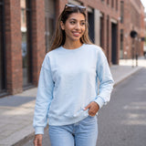 Smiling on a brick lined pavement in a powder blue sweatshirt tucked into light jeans