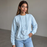 Sky blue sweatshirt with the mini pouch hanging at the chest, worn against a plain wall