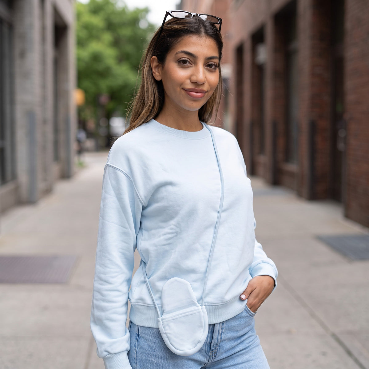 Woman in a light blue crew neck sweatshirt with a matching oval pouch on a city street