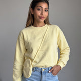 Pastel yellow sweatshirt with a tonal crossbody pouch at the hip, grey studio backdrop