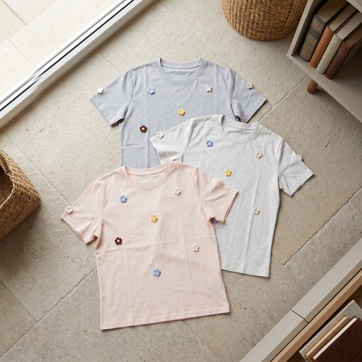 Three crochet flower applique t-shirts in grey, cream and blush pink laid flat