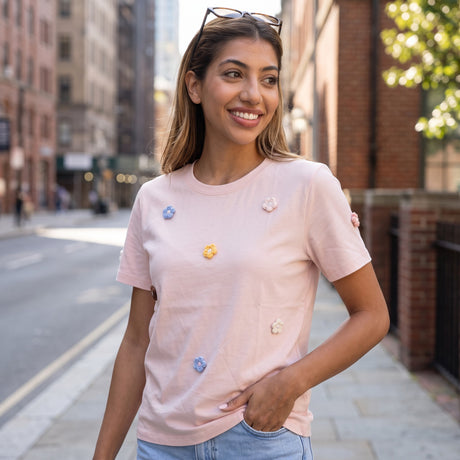 Blush pink tee with crochet daisies worn on a city street