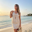 Woman in a lace dress standing on a beach with ocean and sunset in the background