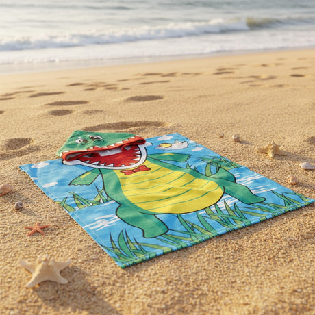Green crocodile hooded poncho towel with a toothy snout and yellow belly flat lay on sand