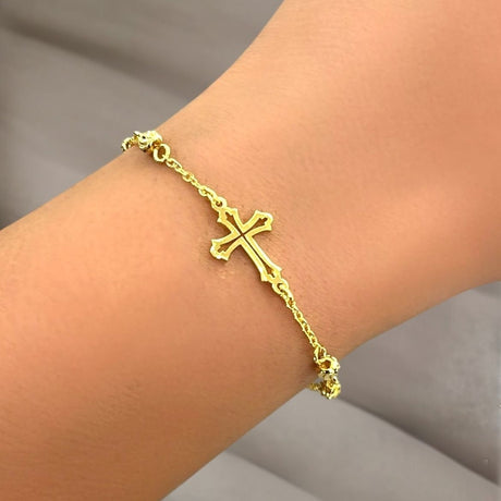 Gold cross bracelet on a wrist with a neutral background