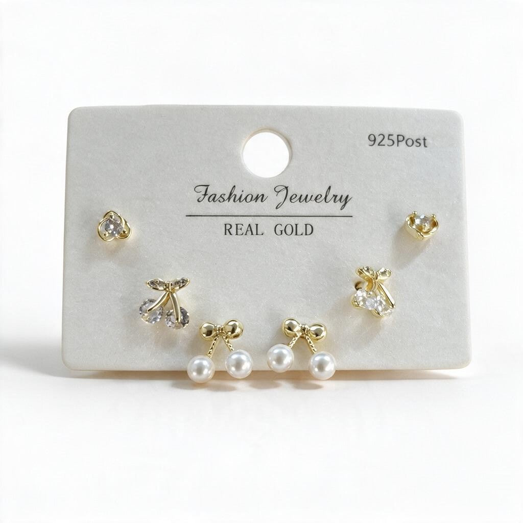Gold tone cherry, round crystal and pearl bow stud earrings on a white display card