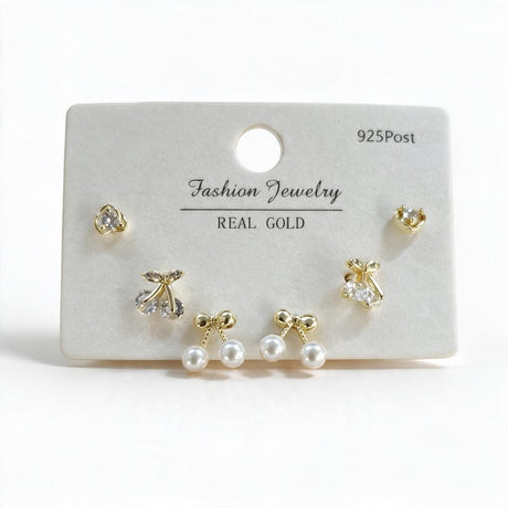 Gold tone cherry, round crystal and pearl bow stud earrings on a white display card
