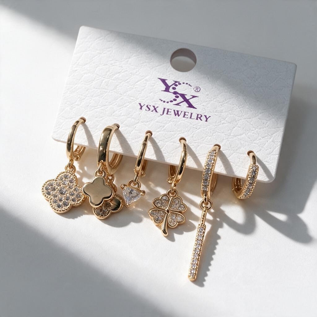 Six single gold huggie earrings with crystal clover, heart and long pave bar drops on a card