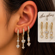 Ear wearing three gold pave huggies with long crystal drops ending in heart shaped stones