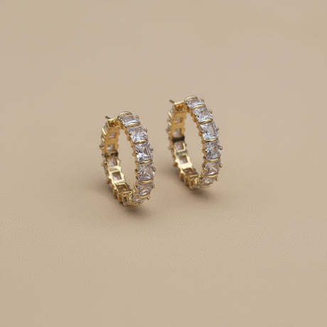 Gold crystal hoop earrings on a beige background