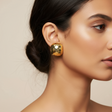 Close-up of a woman wearing gold cube earrings with a neutral background