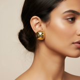 Close-up of a woman wearing gold cube earrings with a neutral background