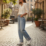 Woman walking on a street wearing blue cuffed jeans and a light-colored shirt