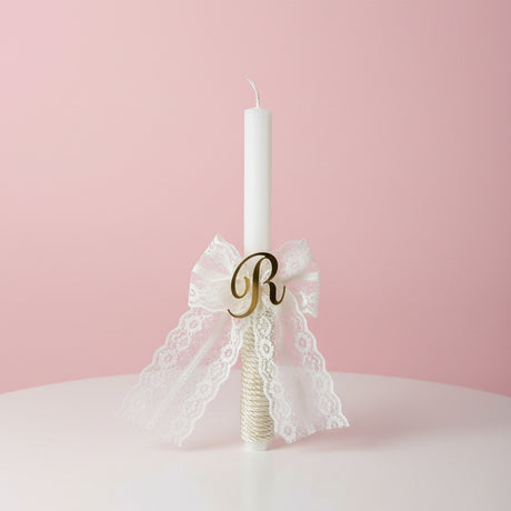White candle with a long cream lace bow and gold letter R