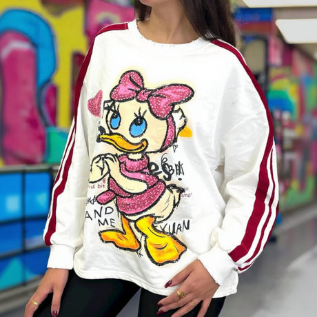 Person wearing a white sweatshirt with a duck cartoon character design in front of colorful graffiti