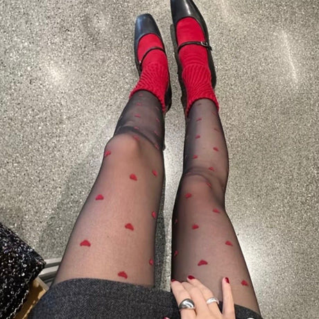 Red heart-patterned tights with black shoes on a concrete surface