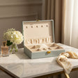 Pale blue jewelry box open to show five necklace pegs, an elastic pouch and a ring cushion