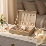 Champagne jewelry box open with gold necklaces on the lid hooks and rings in the tray