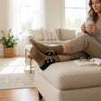 Woman sitting on a couch with feet up, wearing brown socks with black puppy prints, in a bright living room