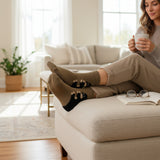 Woman sitting on a couch with feet up, wearing brown socks with black puppy prints, in a bright living room
